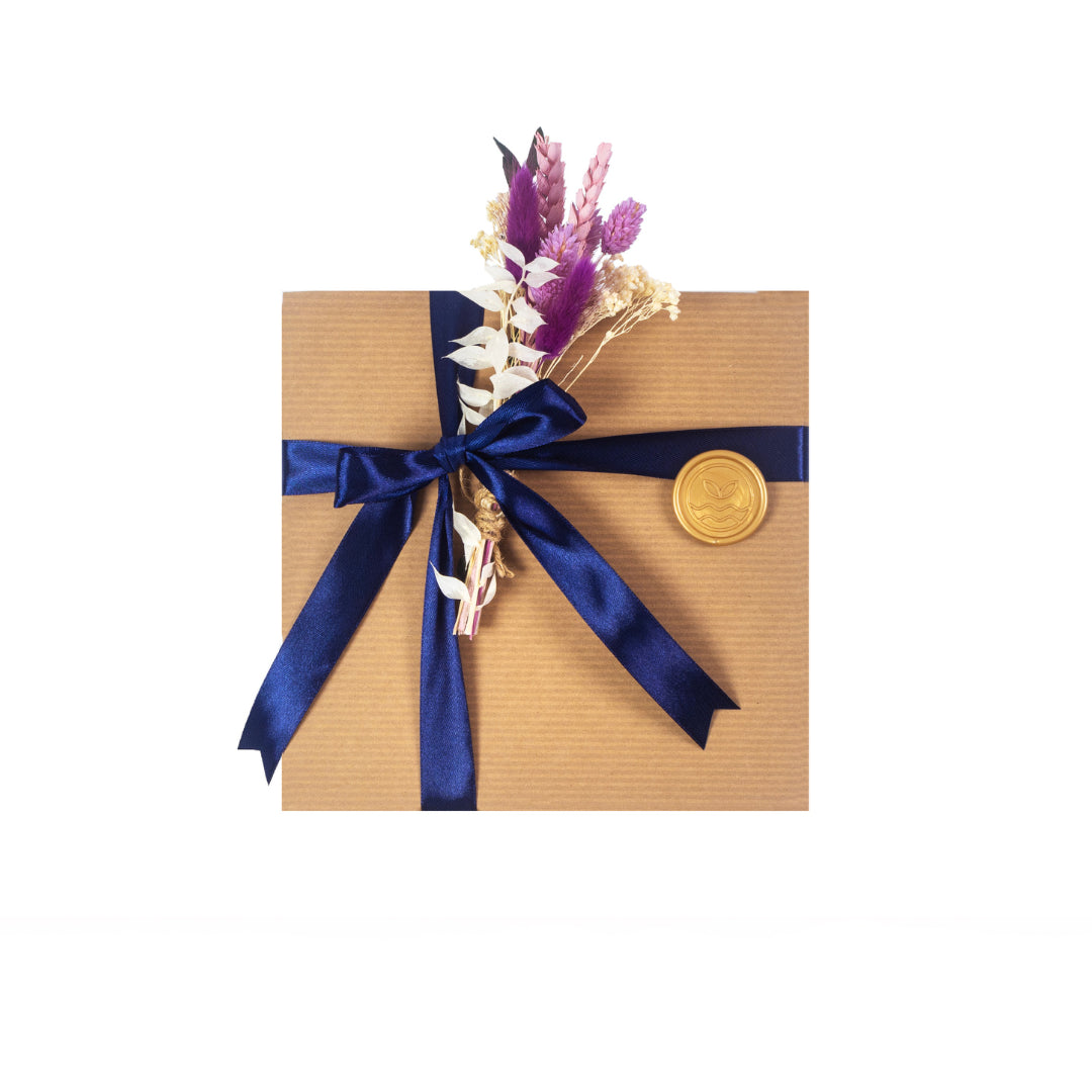 Exterior of the gift kraft gift box with a blue ribbon, gold stamp and seasonal greenery