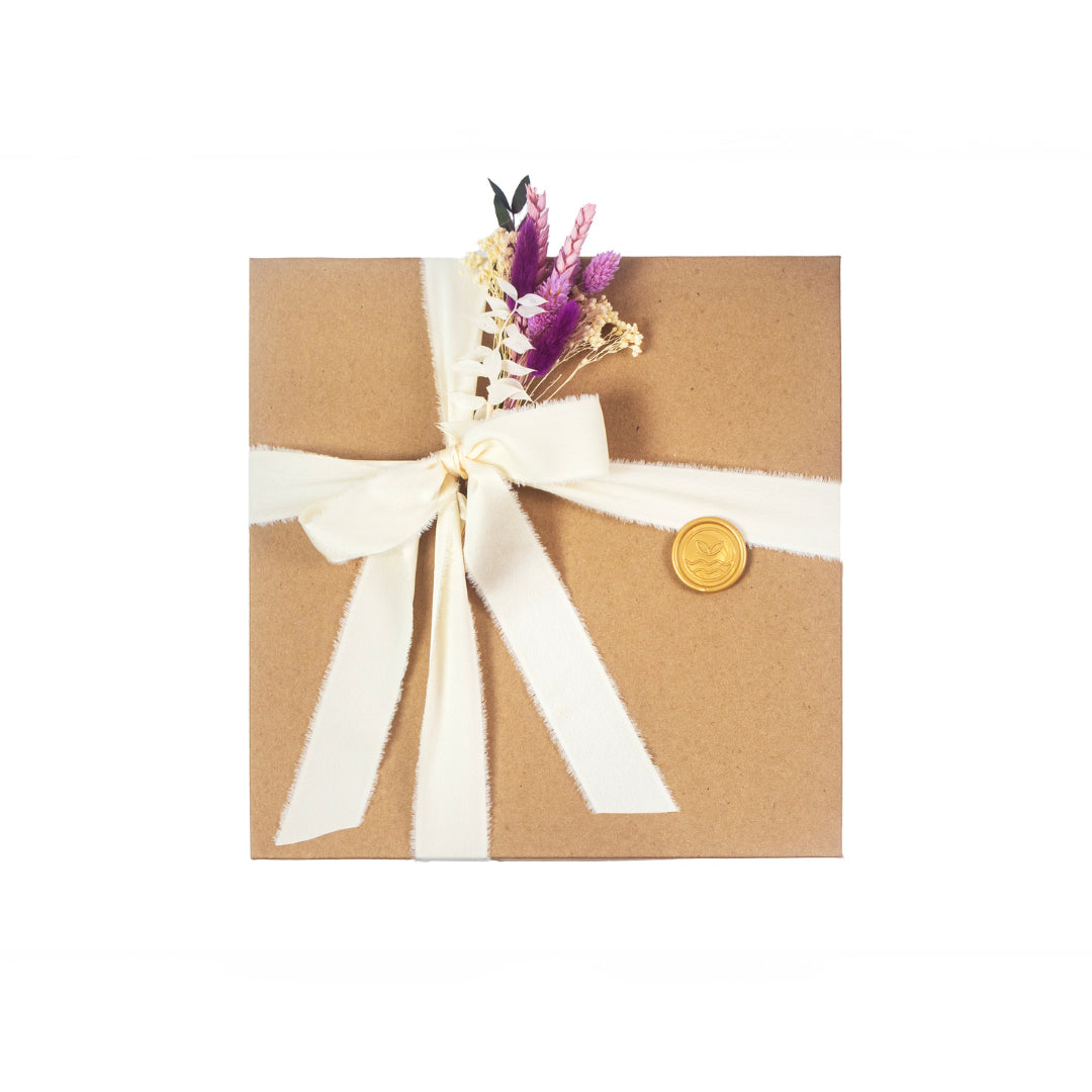 Kraft gift box with white chiffon ribbon, purple and pink flowers and gold stamp.
