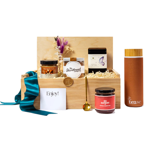 Tea Lovers Executive Gift Box with Gourmet Local Products: Wooden box filled with sustainable, locally curated items including artisanal shortbread, raspberry jam, loose-leaf tea, eco-friendly tumbler, and a gold tea spoon. Decorated with teal ribbon and dried flowers, perfect as a luxury gift for employees or clients.