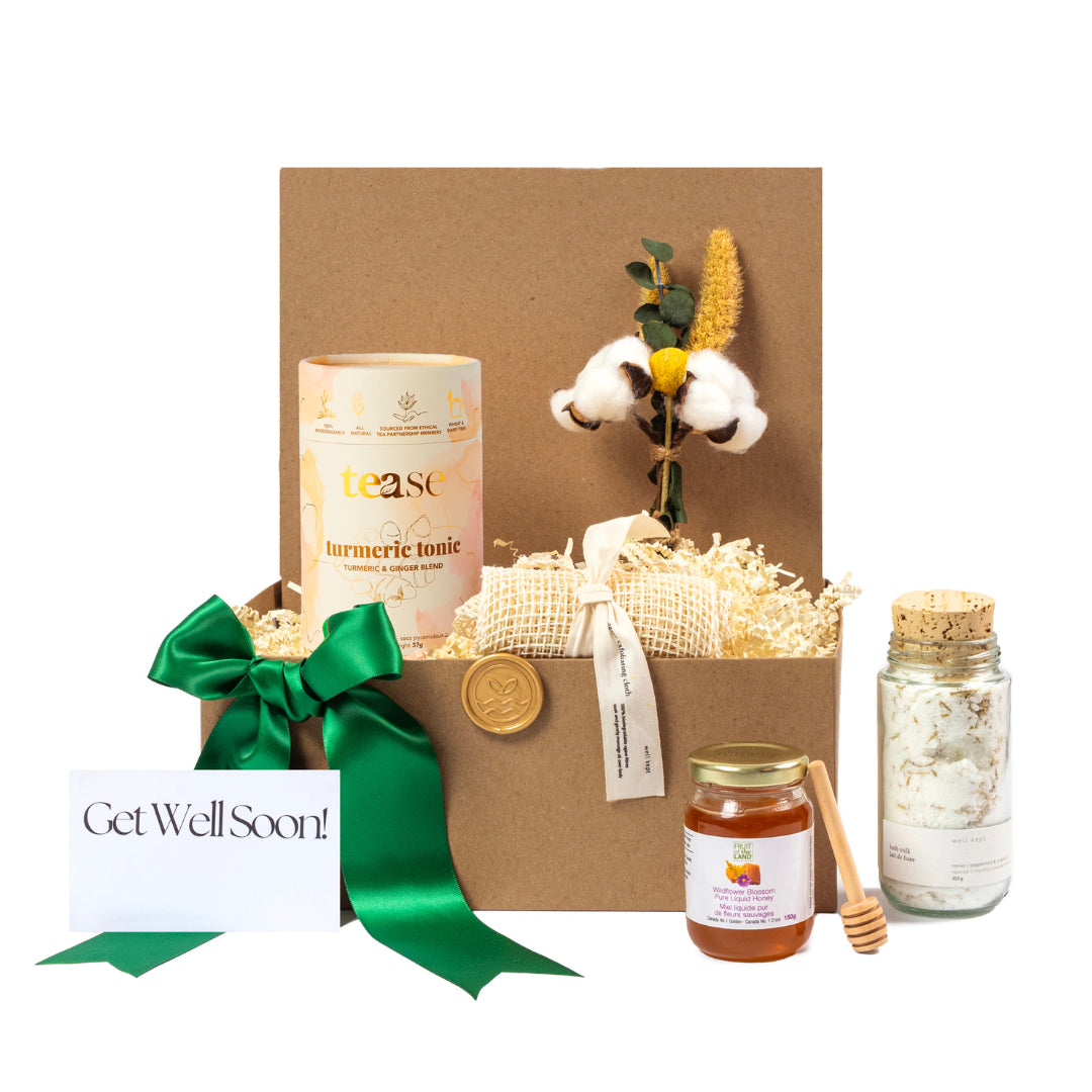 Eco-friendly Get Well Soon gift basket with turmeric tonic, cotton flower bouquet, honey jar with dipper, natural bath salts in corked glass bottle, and sustainable packaging with green ribbon and personalized card. Curated with locally sourced products from small businesses for a thoughtful, plastic-free recovery gift.