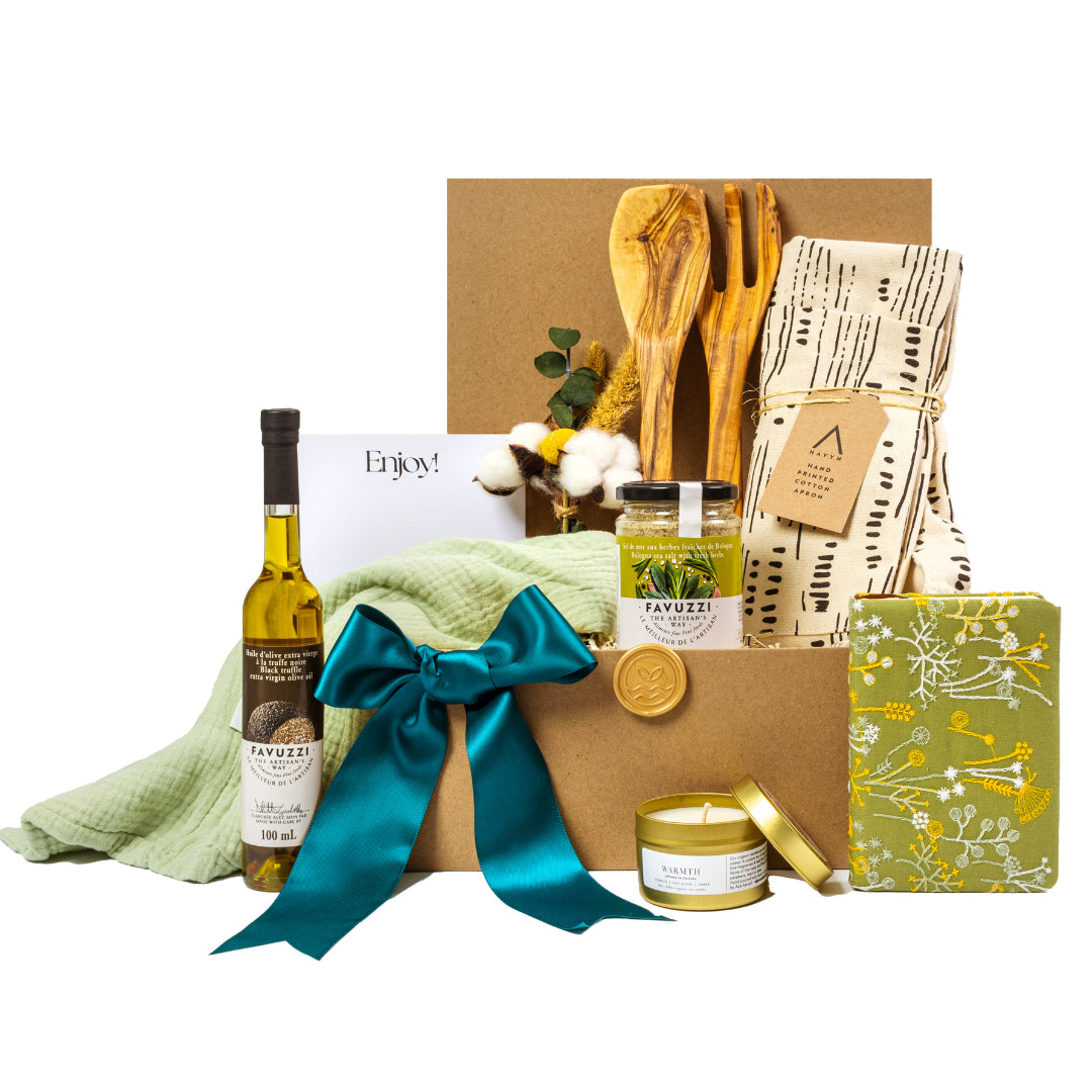 Premium olive oil gift set with sustainable packaging, featuring a bottle of artisanal olive oil, handcrafted wooden utensils, organic cotton apron, gourmet herb blend, scented candle, and a beautifully patterned notepad. Decorated with a teal ribbon and an 'Enjoy!' note, perfect for culinary enthusiasts, corporate gifting, or special occasions. Curated by a Toronto-based, women-owned small business focused on eco-friendly, zero-waste practices