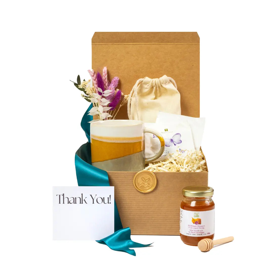Eco-friendly gift basket featuring a handmade ceramic mug, wildflower honey jar with a wooden honey dipper, herbal tea, natural bath soak, dried flower bouquet, and a 'Thank You' card, elegantly presented in a recyclable kraft box with teal ribbon. Ideal for sustainable gifting in Toronto, curated from local small businesses.